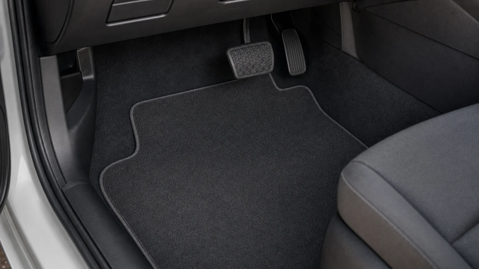 Empty vehicle footwell showing pedals and a fitted floor mat.
