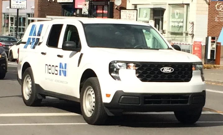 White 2025 Ford Maverick with commercial graphics driving in Montreal